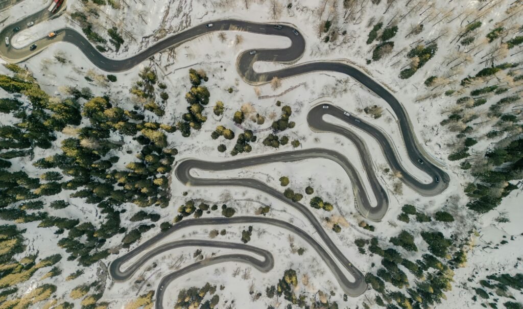 Aerial shot of winding mountain roads surrounded by snowy forest, showcasing winter landscape beauty.